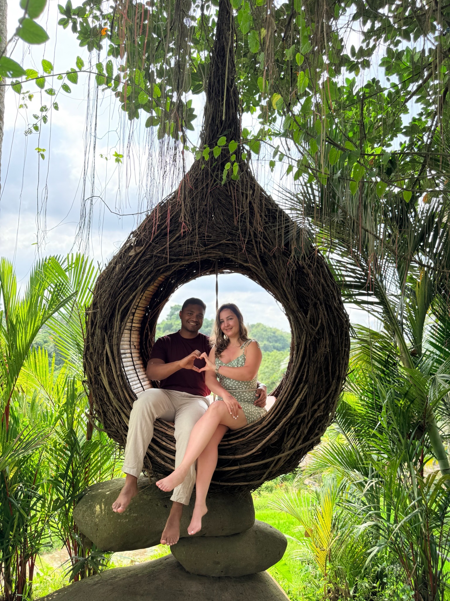 Abhishek and Giselle sitting together in a woven nest surrounded by tropical greenery