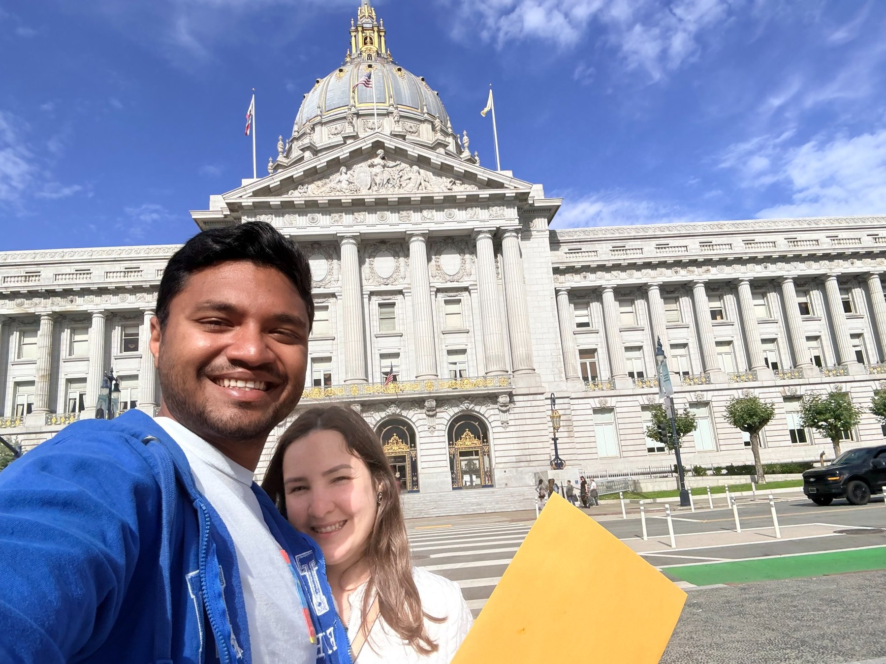 Giselle and Abhishek holding their marriage-license envelope outside San Francisco City Hall